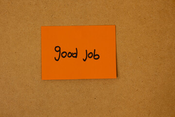 Orange sticky note paper with text saying good job written on it, stuck on a brown board, concept...