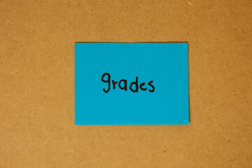 Blue sticky note paper with text saying grades written on it, stuck on a brown board, grades concept