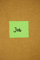 Vertical image of green sticky note paper with text saying job written on it, stuck on a brown board, work concept