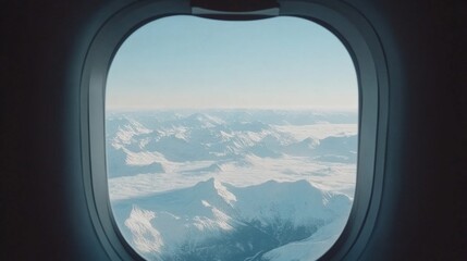 Fototapeta premium Airplane window shot of snow-capped mountains and expansive wilderness below. 