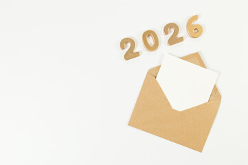 2026 Happy New Year. Top view of gold numbers, brown kraft envelope, white card on white background. Copy space, flat lay.