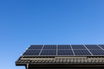 Fototapeta premium House with solar panels photovoltaic plant system professionally installed on metal sheet roof, go green. Clear blue sky background. Clean alternative energy power concept, sustainable resources