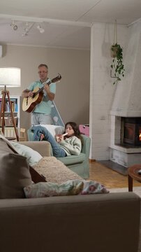 A middle-aged man and a 12-year-old girl enjoying a musical moment together, with him playing guitar and her playing a recorder flute in a cozy setting