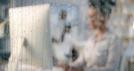 Rain, office and window with work of woman at computer for digital update of website at job. Blur, drops and glass with professional web design employee at social media and creative agency in winter