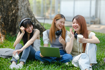 Three young women are sitting on the grass, laughing and smiling