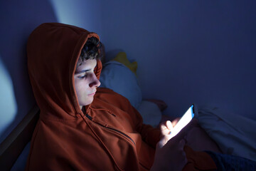 Teenager using a smartphone lying in bed late at night, playing games, watching videos online, and scrolling the screen. Children's screen addiction. Screen Addiction in Youth