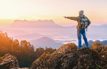 Male hiker with backpack points to the top rock mountain landscape and beautiful view sunset...