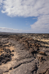 White sand beach with solidified volcanic lava flows, black rocks. Mountains in the background and sky with big white clouds. Caletón Blanco, Lanzarote, Canary Islands, Spain