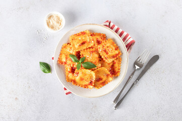 Ravioli with ricotta cheese, fresh tomato sauce and fresh basil on a gray background. Top view.