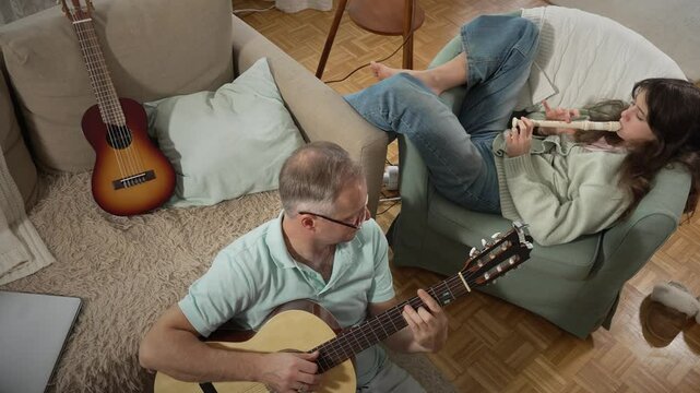 A middle-aged man and a 12-year-old girl enjoying a musical moment together, with him playing guitar and her playing a recorder flute in a cozy setting