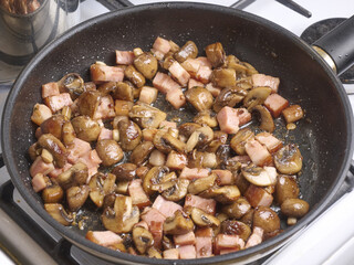 Sliced ​​fried mushrooms with bacon in a large frying pan. Cooking pasta with mushrooms and bacon. Classic Italian cuisine. Cooking Italian dishes at home
