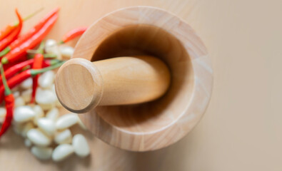 Top view close-up of wooden mortar and pestle over garlics and peppers on a wooden