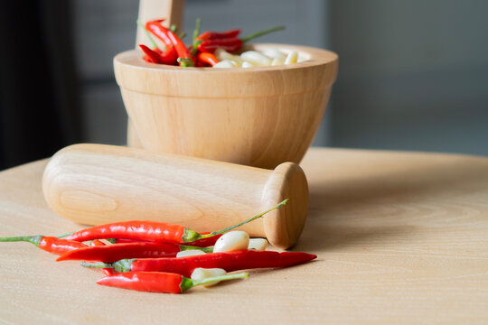 Wooden mortar and pestle with red pepers and some of garlics prepared for making herbal dishes.