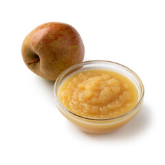 Glass bowl with organic homemade apple sauce and a fresh apple isolated on white background close up