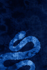 藍染めの背景に映える、絞り染めで描いた「2025」干支のヘビ