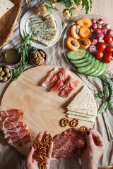 a person serving charcuterie board a platter of meat cheese crackers nuts olives and vegetables
