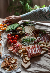 a person serving charcuterie board a platter of meat cheese crackers nuts olives and vegetables