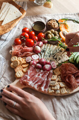 a person serving charcuterie board a platter of meat cheese crackers nuts olives and vegetables