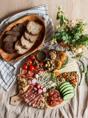 a person serving charcuterie board a platter of meat cheese crackers nuts olives and vegetables