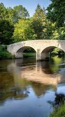 A stone bridge arches over a calm river, reflecting the surrounding lush greenery.