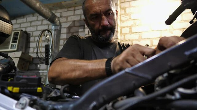 Male repairer fixing motor of motorbike using tool at workplace. Professional mechanic repairing engine of motorcycle at workshop. Adult repairman working at garage. Concept of maintenance service