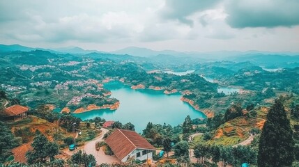 Fototapeta premium A picturesque view of a lake surrounded by lush green hills, with a few houses nestled into the landscape. The sky is overcast with clouds, adding to the serene atmosphere.