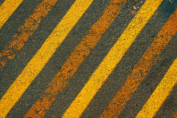 Diagonal yellow caution strip lines painted on black asphalt surface