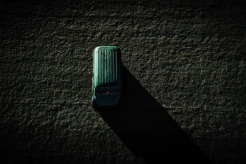 A green car parked on a grassy field, viewed from directly above, casting a long shadow in the sunlight.