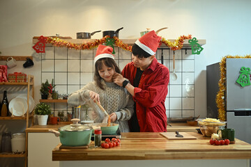 Happy young couple wearing Santa hats cooking special meal on Christmas day