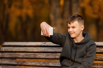 A teenage boy sits on a bench with his arms stretched along the backrest, eyes closed, fully...