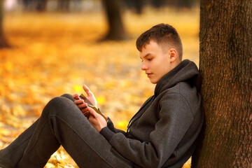 A teenage boy sits on a bench with his arms stretched along the backrest, eyes closed, fully...