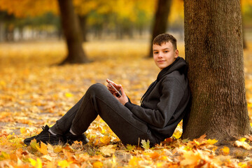 A teenage boy sits on a bench with his arms stretched along the backrest, eyes closed, fully...