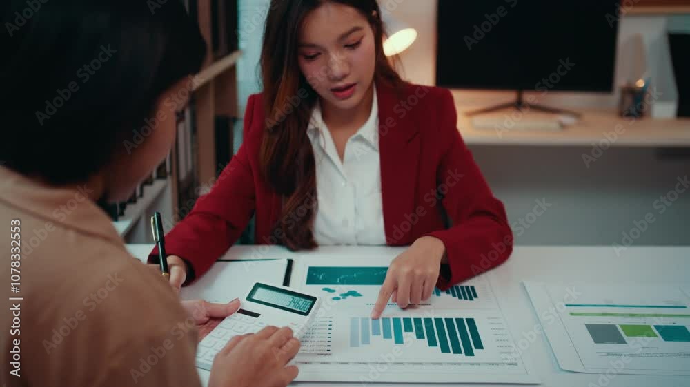 Aufkleber two asian businesswomen analyze financial charts and use a calculator in their office at night, enga