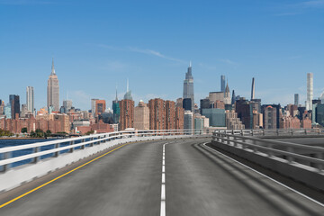 Fototapeta premium Road curving towards Manhattan skyline with skyscrapers in view under a clear blue sky.