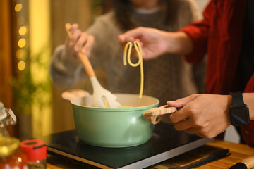 Close up of couple cooking pasta together in a warm kitchen during the festive season