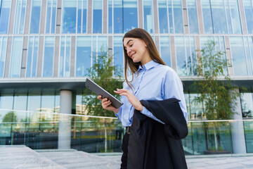 Young Professional Woman Using a Tablet Outside a Modern Office Building on a Sunny Day