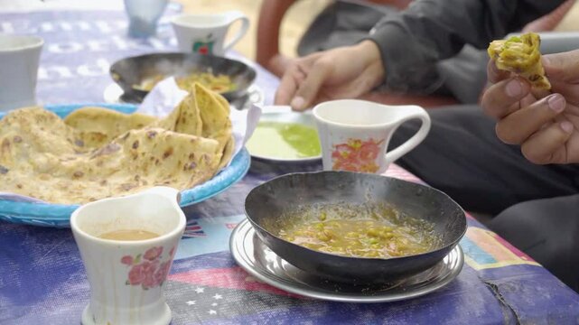 At a charming local dhaba, people relish a delightful breakfast featuring warm, crispy parathas served alongside a flavorful omelet, and refreshing raita.
