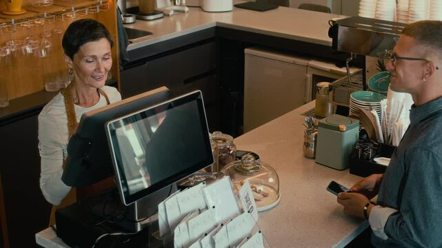 High angle view of young Caucasian man ordering coffee in modern cafe and paying for it with credit card