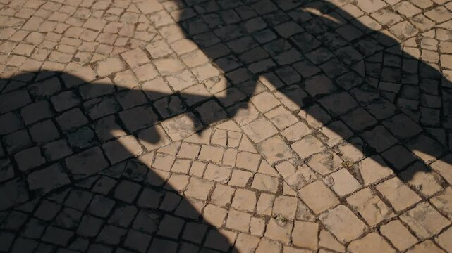 Shadows of a couple holding hands on cobblestone pavement, symbolizing unity and romance