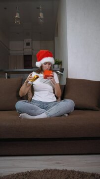 Woman in Santa hat sitting on sofa opening christmas gift. Frustration washes over her face as she opens contents inside, leading to moment of sadness, she is dissatisfied. vertical video
