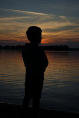 silhouette of a boy against the backdrop of sunset on the lake