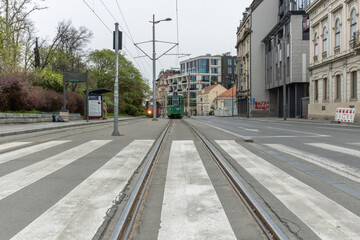 Train is traveling down a street with a crosswalk