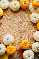 circular arrangement of white and orange mini pumpkins on a woven mat, accented with autumn leaves. A cozy and seasonal setup for fall or Thanksgiving decor.