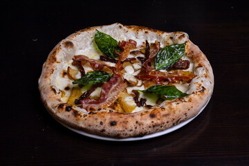 Pizza tradizionale napoletana con mozzarella, melanzane, patate al forno, pancetta croccante e basilico fresco servita in una pizzeria elegante