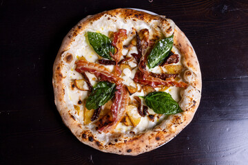 Pizza tradizionale napoletana con mozzarella, melanzane, patate al forno, pancetta croccante e basilico fresco servita in una pizzeria elegante