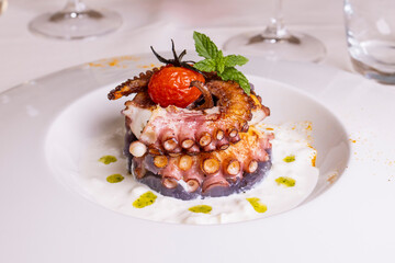 Polpo cotto alla brace e servito su una crema al latte con gocce di pesto di basilico in un ristorante elegante