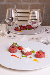 Tavola di un ristorante elegante apparecchiato con tovaglia, bicchieri e posate e con due antipasti dic Arne cruda serviti