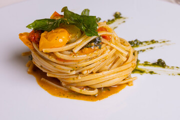 Spaghetto ai tre pomodori, rosso, giallo e nero, condito con, basilico e pepe e servito in un ristorante elegante