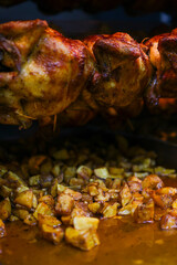 Pollo allo spiedo in cottura con patate al forno in cottura sotto che ricevono il grasso del pollo quando cola