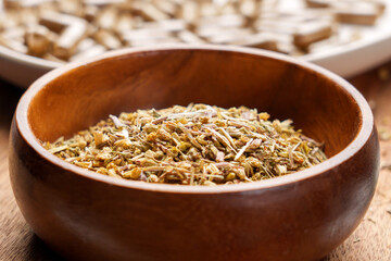 Wooden bowl filled with dried medicinal herbs next to herbal tablets, blending Ayurveda and modern herbalism for natural supplements and wellness science